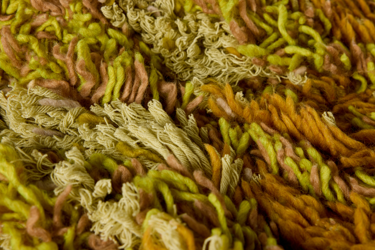Close-up of the shaggy texture twisted fibers in olive green, mustard yellow, tan, and muted pink-brown tones.