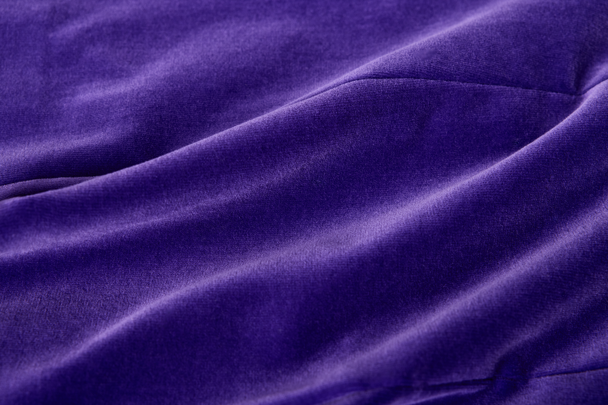 A close-up of draped purple velvet fabric with soft folds and a smooth, slightly lustrous texture.