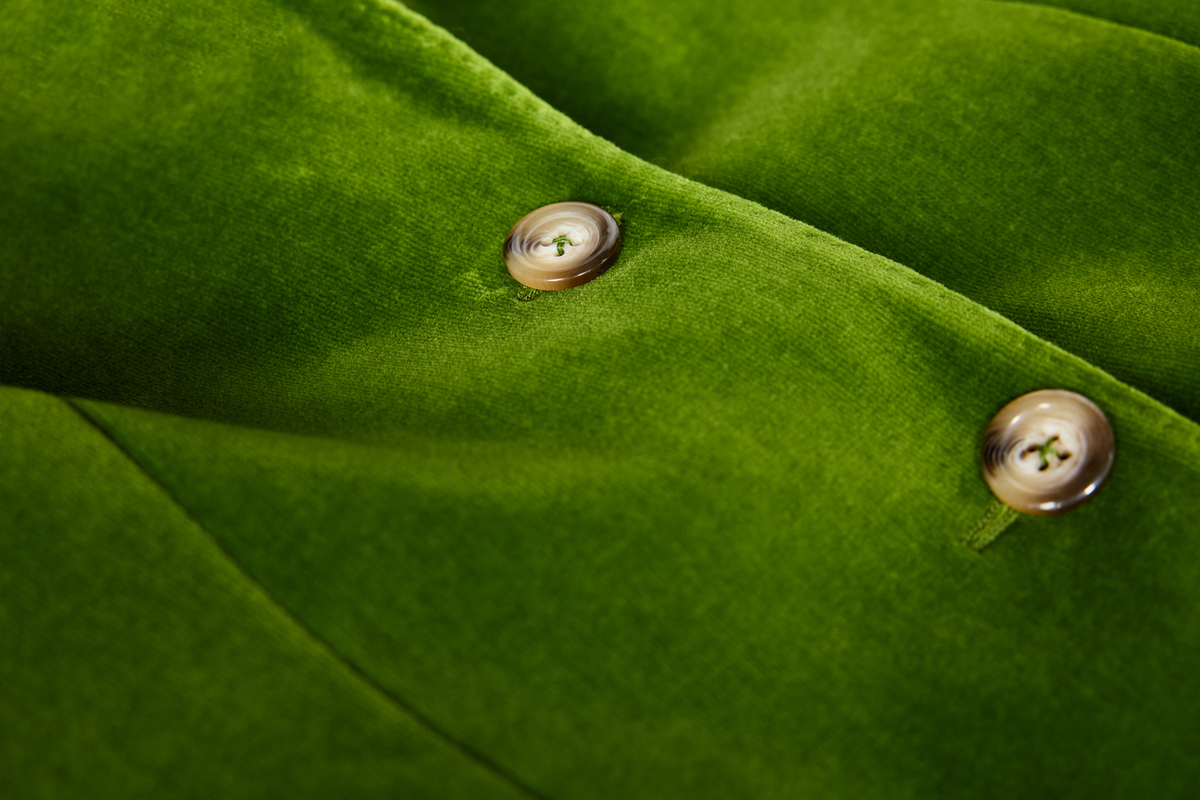 Close-up of a green velvet fabric surface with two metallic buttons on a button placket.