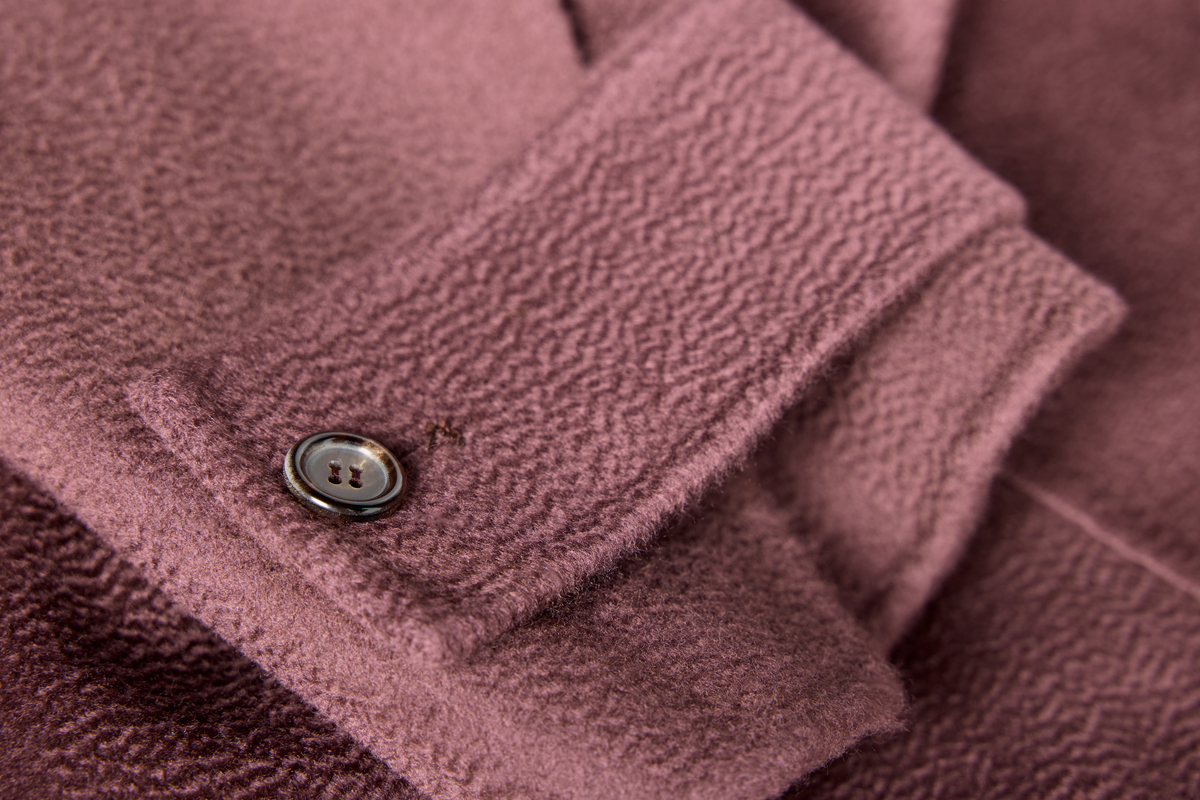 Close-up of a dusty rose textured fabric garment with a single metal button on a folded cuff.