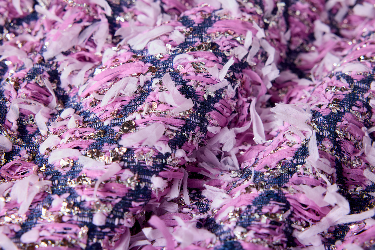 A close-up of a chunky fabric with a textured, frayed weave in pink, navy blue, and white, accented with shimmering sequins.
