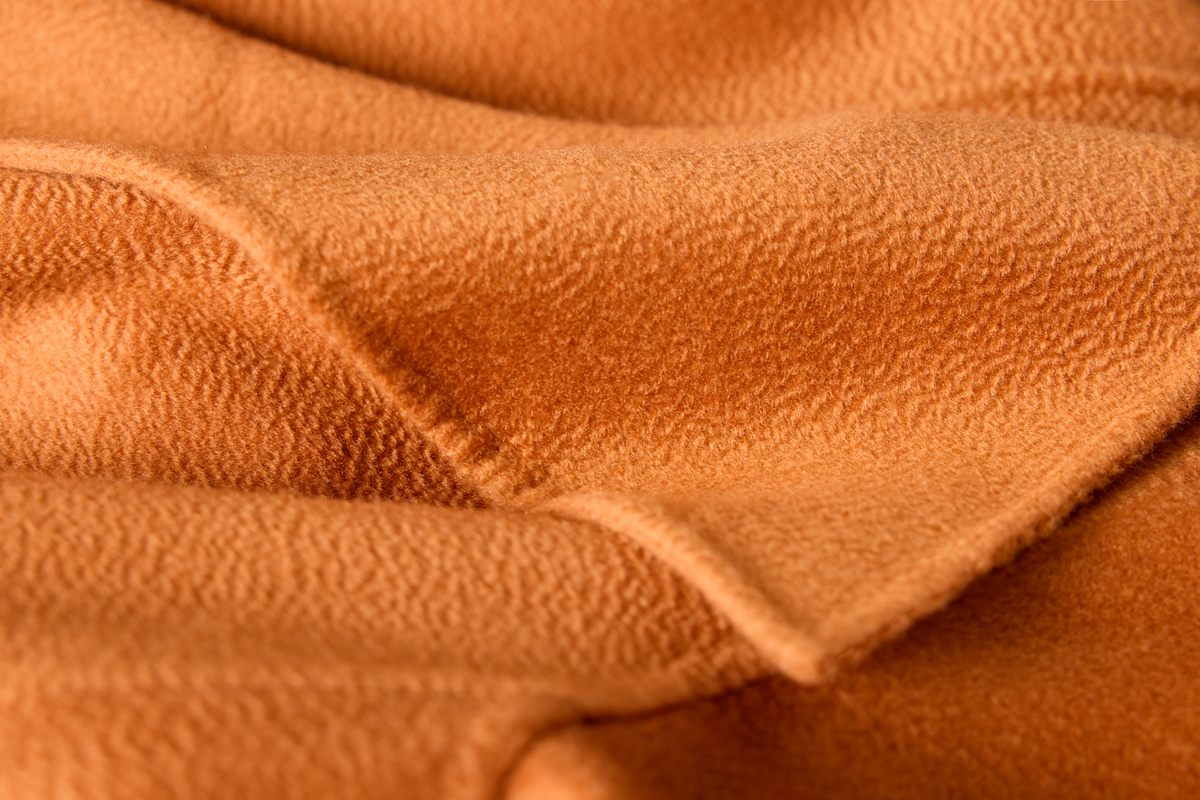 Close-up of a soft, textured fabric in a warm camel or tan color, showing the fine woven material and gentle folds.