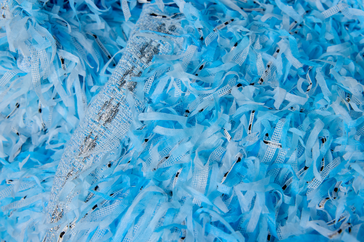 A close-up of shredded light blue strips with a few small black flecks visible throughout.