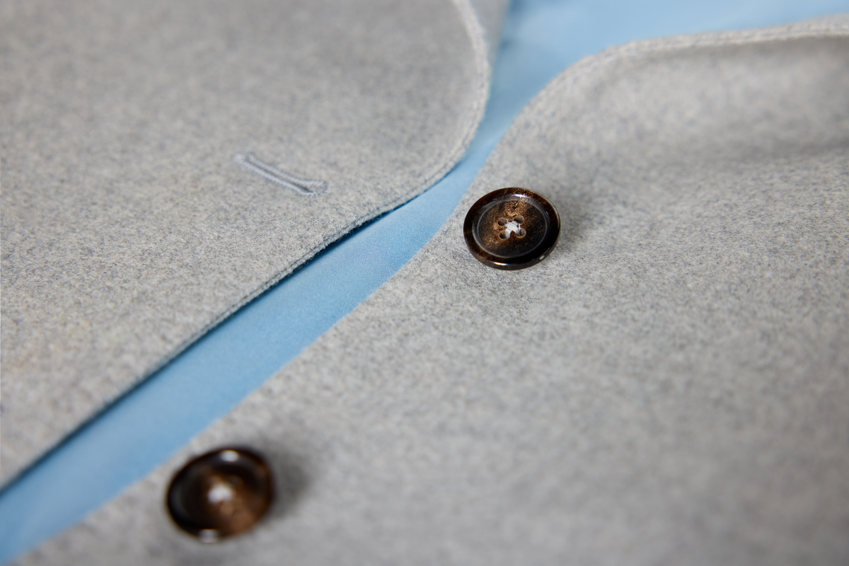 Close-up detail of a light gray wool-blend jacket or coat with dark brown buttons.